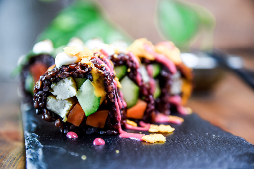 4 vegane Crunchy Zucchini Signatire Sushi Rolls auf einer schwarzen Schieferplatte